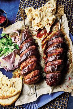 an assortment of meats and vegetables on a platter with pita bread, salsa, and tortillas