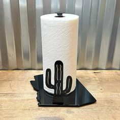 a black and white toilet paper holder with a cactus design on the top, sitting on a wooden table