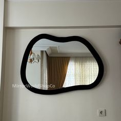 a mirror that is on the wall in front of a window with curtains behind it