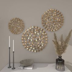 three circular metal wall art pieces on a gray wall next to a vase and candle