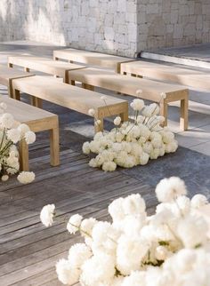 white flowers are sitting on wooden benches in front of a brick wall and concrete floor