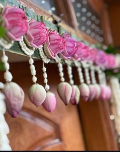 pink and white flowers are hanging from the side of a wooden door with beads on it