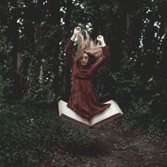 a woman in a red dress is flying through the air over an open book with her hands above her head