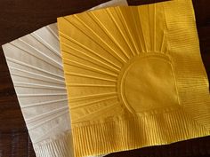 two yellow napkins sitting next to each other on top of a wooden table,