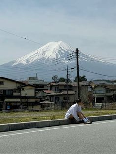 a man sitting on the side of a road next to a tall white snow covered mountain