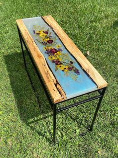 a table with flowers painted on it sitting in the grass next to some metal legs