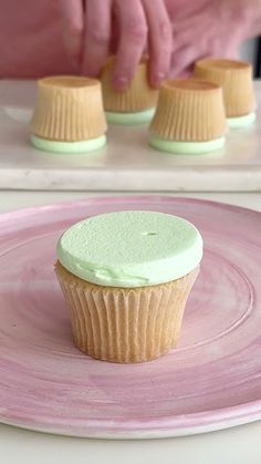 someone decorating cupcakes with green frosting on a pink and white plate