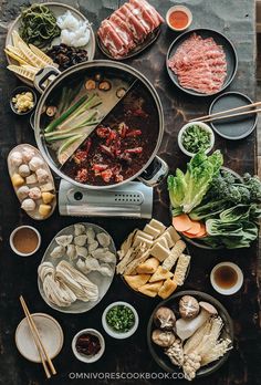 a table topped with lots of food and chopsticks next to bowls filled with meat