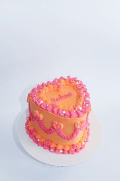 a heart shaped cake with pink and orange frosting on a white plate against a white background