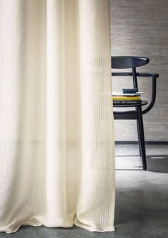 a chair sitting next to a white curtain in front of a table with a book on it