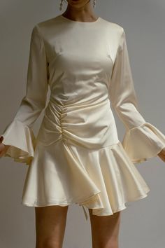 a woman wearing a white dress with long sleeves and ruffles on the skirt