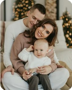 a man and woman sitting on a couch with a baby in their lap, smiling at the camera