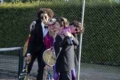 four people standing on a tennis court holding racquets and posing for the camera