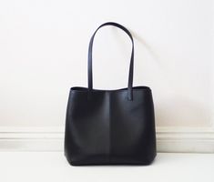 This simple tote features black vegan (fake) leather, magnet top closure and internal pockets. Details:-Dimensions: 12" length (top to bottom), 10" bottom width, 7" depth, 10" X 7" base (bottom)-Each shoulder strap measures approximately 23" full length-Black vegan (fake) leather-Fabric interior lining (solid black) - color can be customized-Internal pockets: 1 slip pocket, 1 zippered pocket-Magnet top closureBecause each bag is made by hand, the measurement is approximate and may vary slightly Everyday Bucket Bag With Magnetic Closure, Modern Medium Shoulder Bag For Shopping, Minimalist Everyday Bags With Magnetic Closure, Sleek Black Satchel For Everyday Use, Chic Medium Black Bag, Chic Black Medium-sized Bag, Minimalist Work Bag With Magnetic Closure, Minimalist Shoulder Bag With Magnetic Closure For Daily Use, Elegant Medium Black Bag