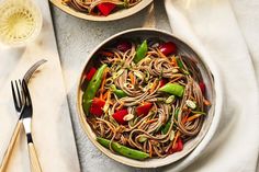 two bowls filled with noodles and veggies on top of a white table cloth