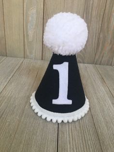 Please read shop announcement for current processing times and updates. Your birthday boy will look absolutely adorable in this mini birthday hat for his half birthday or whole birthday! Perfect for a party or photo shoot. This hat is available as a mini size (5 inches tall by 4 inches wide) Or a full size (7 inches tall by 5 inches wide). It features black felt with a white number of your choice. White mini pom pom ribbon is attached along the base of the hat with a yarn Pom Pom on top. It has Cute White Hat For First Birthday, Cute White Hat For Birthday, White Birthday Party Hat Supplies, Playful White Hat For First Birthday, Playful White Hat For Birthday, Playful White Hats For Birthday, Fun White Birthday Hat, Playful White Birthday Hat, Playful White Party Supplies For First Birthday