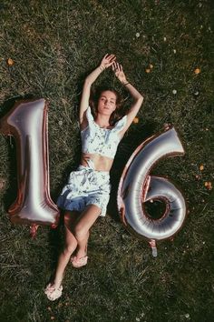 a woman laying in the grass next to balloons that say'16'and number sixteen