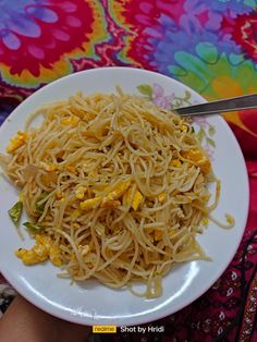 a white plate topped with noodles and vegetables on top of a colorful cloth covered table