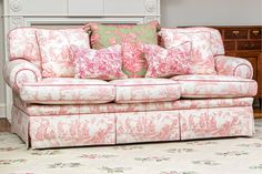 a couch with pink and green pillows on it in front of a white fireplace mantel