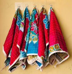 four red and blue cloths hanging from hooks on a yellow wall in the kitchen