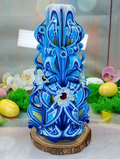 a blue and white vase sitting on top of a wooden stump in front of flowers