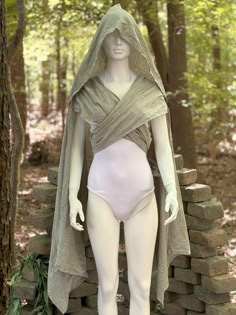 a mannequin wearing a white bodysuit and cape in front of a stone wall