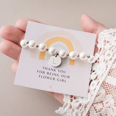 "Surprise your sweet flower girl with our adorable flower girl bracelet - a wonderful thank-you gift! This child-sized bracelet features alternating gold-plated beads between each faux pearl, adorned with a dainty monogram charm available in gold or silver for that extra touch of personalization. Elegantly packed with a thank-you card featuring a cute rainbow design and a gift box, these stretchy bracelets are designed to fit most girls aged 3-10. They make for an ideal keepsake, expressing your Adjustable Charm Bracelet For Bridesmaid Gift On Mother's Day, White Flower Bracelet For Mother's Day, White Flower Bracelets For Mother's Day, Cute White Pearl Bracelet For Gift, Cute White Pearl Bracelet Gift, Personalized Charm Bracelet For Bridesmaid Gift On Mother's Day, Personalized Adjustable Pearl Bracelet For Bridesmaids, Personalized Charm Bracelet For Bridesmaids, Cute White Jewelry For Bridesmaid Gift