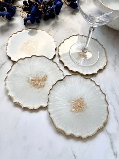 three white plates with gold rims on a marble counter top next to a wine glass