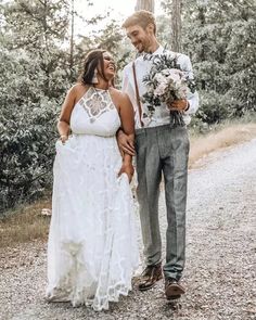 a man and woman standing next to each other on a dirt road in front of trees