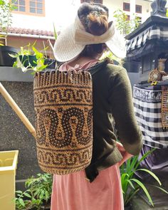 a woman with a large hat on her head is carrying a bag in front of a building