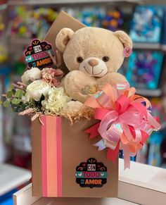 a brown teddy bear sitting inside of a box with flowers and ribbons on it's side