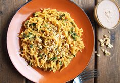 an orange plate topped with pasta and nuts next to a glass of milk on top of a wooden table