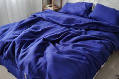 an unmade bed with blue comforter and pillows on it in a white room