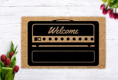 a welcome mat with flowers and tulips in the background on a white wooden surface