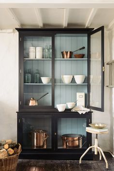 a black china cabinet with glass doors and bowls on the top shelf in front of it