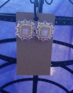 a pair of beaded earrings hanging from a metal hook on top of a piece of cardboard