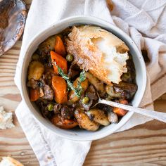 a bowl filled with meat and vegetables on top of a wooden table next to bread