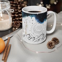 a coffee mug sitting on top of a table next to an orange and some pine cones