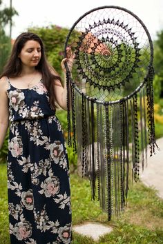 a woman holding up a large metal dream catcher in her hand and standing on the grass