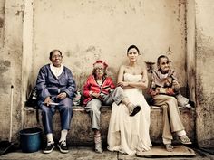 four people sitting on a bench in front of a wall with an old building behind them