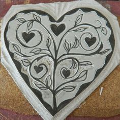 a heart shaped tile with hearts and leaves on it's side, sitting on top of a rock