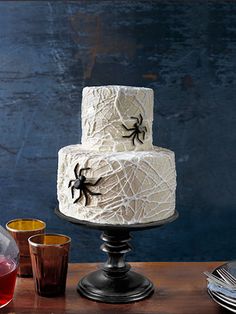 a three tiered cake decorated with black spider webs and candles on a wooden table