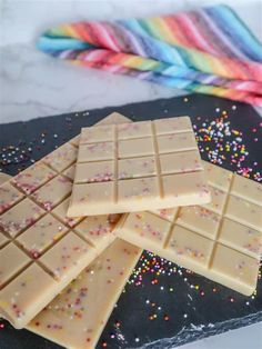 three pieces of white chocolate with sprinkles on a black slate board next to colorful streamers