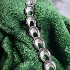 "This vintage silver tone Trifari bracelet is a stunning example of mid-century chain link bracelet styles. With a snap lock fold over clasp, it is secure and comfortable to wear. The horse-shoe shaped links feature a half shiny silver finish and textured silver finish that adds depth and dimension to the piece. At 7.25 inches in length and 0.5 inches in width, this bracelet has a nice weight to it and feels quite sturdy. Additionally, the back of the bracelet has the same textured lines as the front, giving it a polished and finished look from every angle. A unique feature of this bracelet is the Trifari stamp and copyright symbol on the back of the fold over clasp. This suggests that this piece was made in the 1950s-1960s during a time when Trifari was at the forefront of American costum 60s Jewelry Vintage, Retro Silver Metal Bracelets, Silver Retro Metal Bracelets, Vintage Sterling Silver Oval Link Bracelet, Vintage Metal Chain Bracelet With Oval Links, Vintage Oval Link Metal Bracelet, Vintage Metal Oval Link Bracelet, American Costume, 60s Jewelry