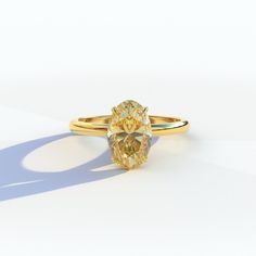 an oval shaped yellow diamond sits on a white surface, with shadow from the ring