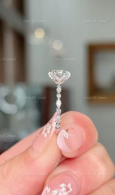 a person holding a diamond ring with white flowers on the middle of their finger and it's setting in front of them