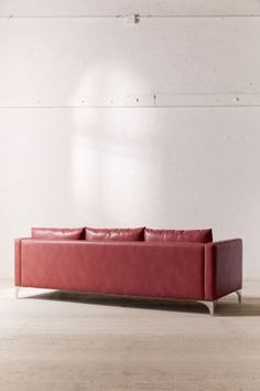 a red leather couch sitting on top of a wooden floor next to a white wall