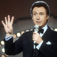 a man in a tuxedo is holding a microphone and making the peace sign