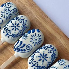 four blue and white decorated lollipops sitting on top of a wooden cutting board