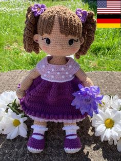 a crocheted doll is standing next to daisies on the ground with an american flag in the background